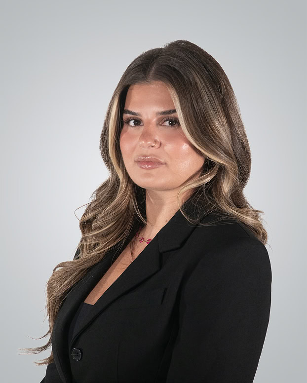 Professional woman in black blazer with long wavy hair, neutral background.